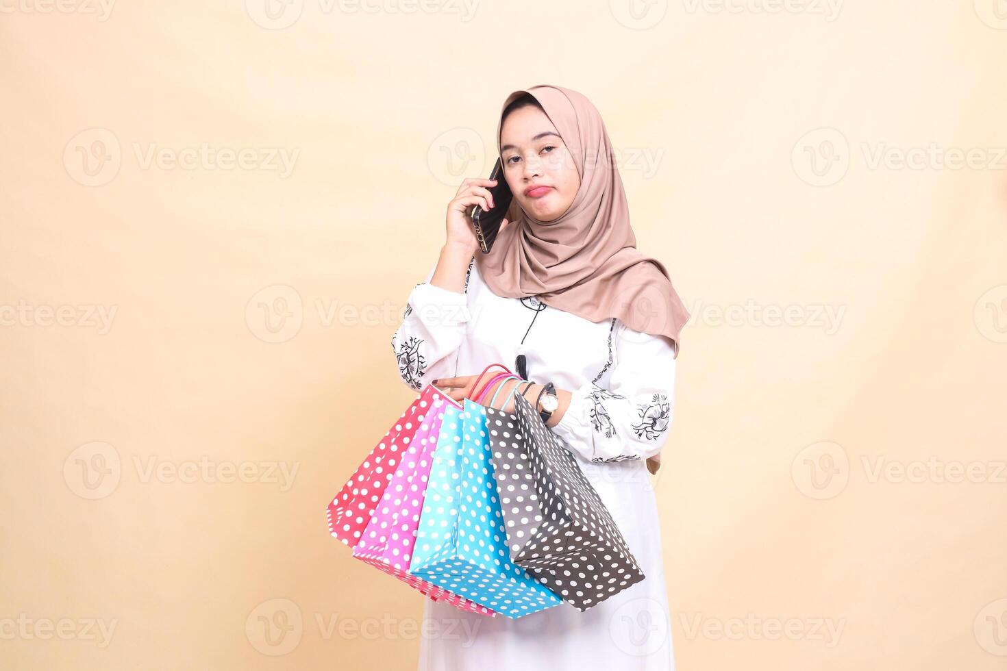 a young Asian Muslim girl in a hijab frowns at someone's phone looking ahead and carrying a paperbag shopping bag. for advertising, technology, Eid and Ramadan photo