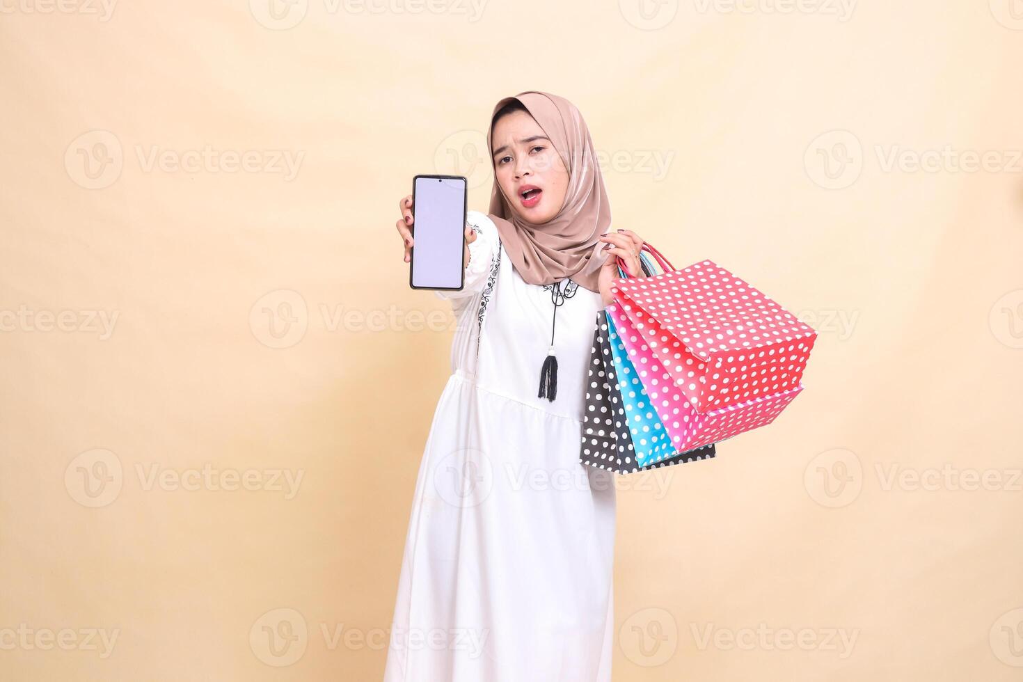 a young Asian Muslim girl wearing a hijab is surprised to frown, showing a cellphone screen and carrying a paper bag. for advertising, technology, Eid and Ramadan photo