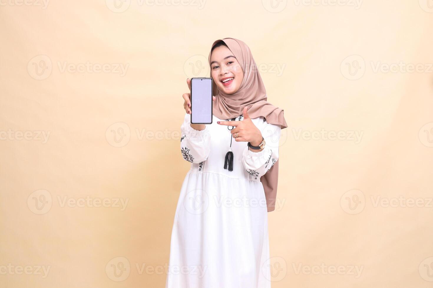An Asian Muslim girl wearing a hijab smiles cheerfully, showing her cell phone gadget screen with a thumbs up gesture okay to create sales content. for advertising, technology, Eid and Ramadan photo