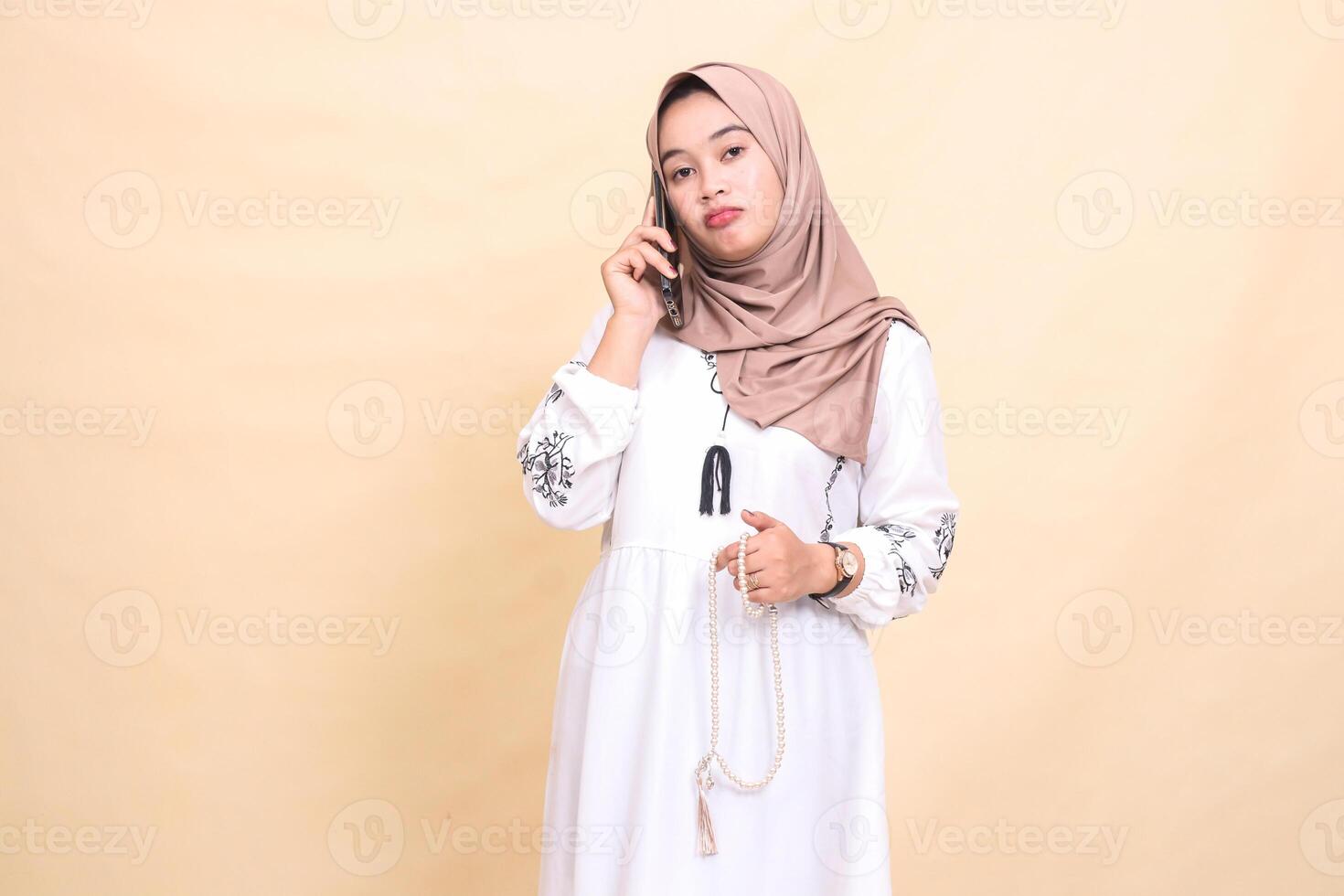 A young Asian Muslim woman wearing a hijab is sullenly holding prayer beads and calling someone. for advertising, lifestyle, banners and Ramadan photo
