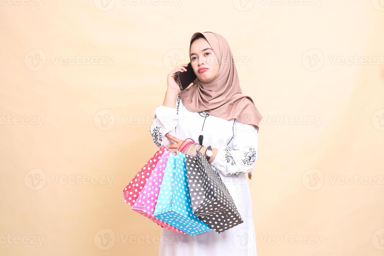 a young Asian Muslim woman in a hijab scowls at someone's phone and carries a paperbag shopping bag. for advertising, technology, Eid and Ramadan photo