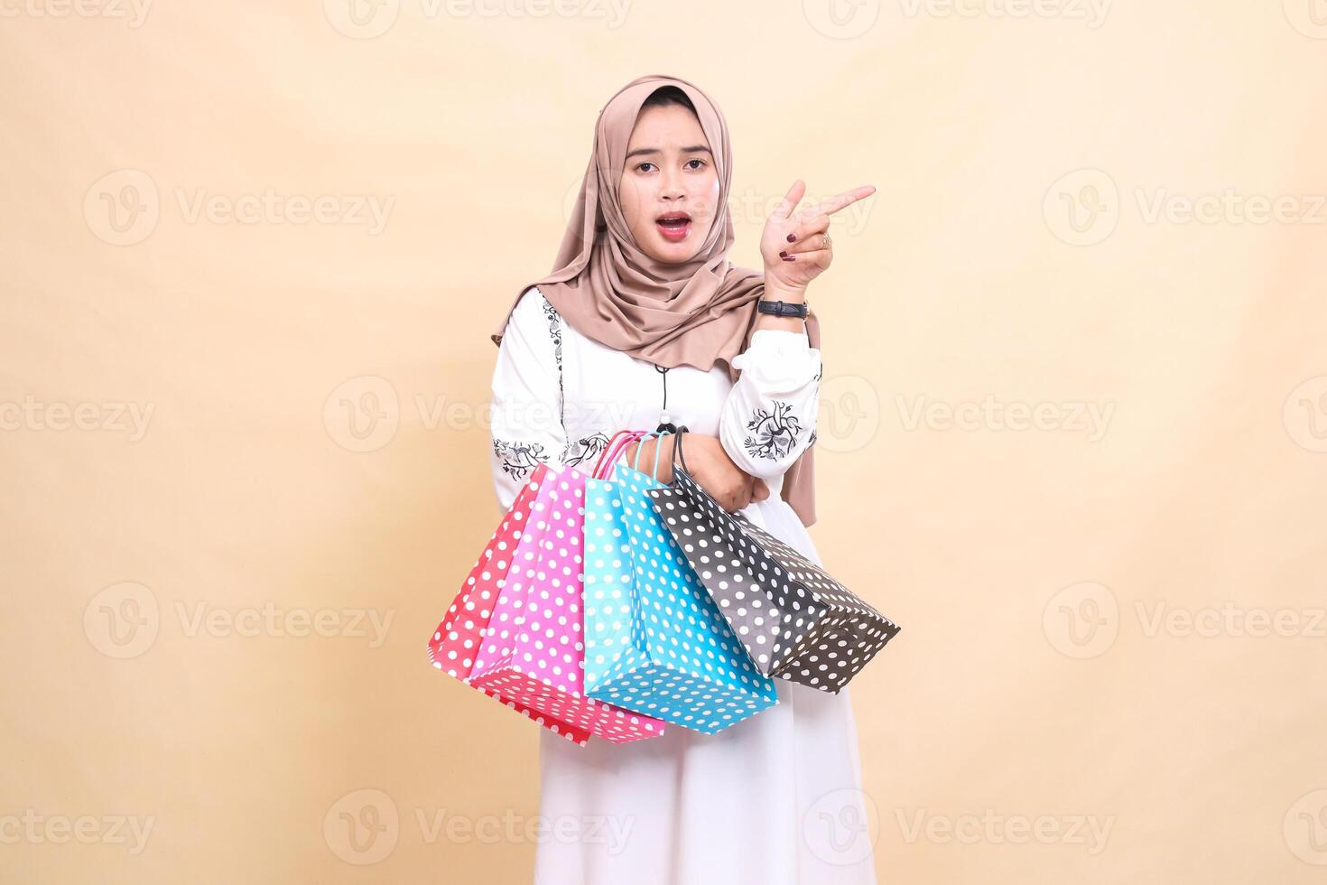 a young Asian Muslim girl wearing a hijab was shocked, pointing to the left and carrying a paper bag. for advertising, culture, Eid and Ramadan photo