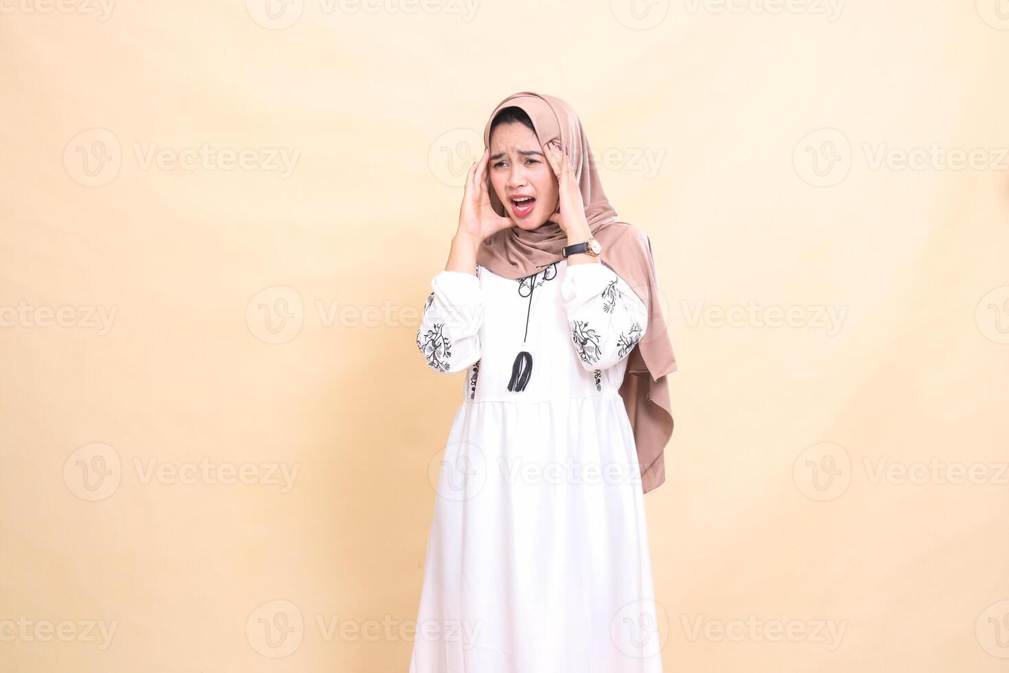 portrait of an adult indonesia Muslim girl wearing a hijab slanted to the right and both sides holding her head and having a severe headache. used for advertising, health, science and Ramadan photo