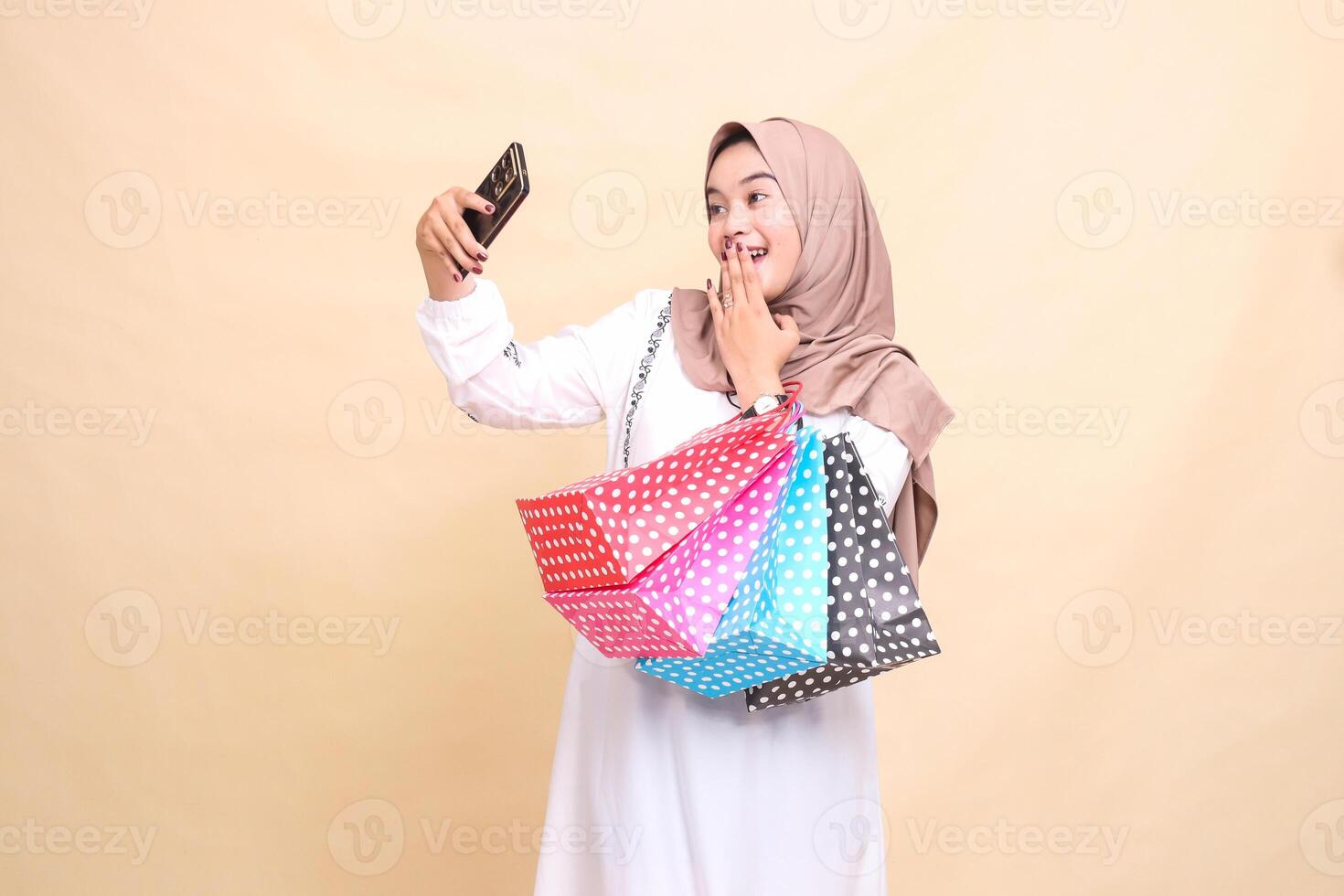 A young indonesia Muslim woman wearing a cheerful hijab is surprised by a call greeting her family via cellphone and carrying paper bags. for advertising, culture, Eid and Ramadan photo