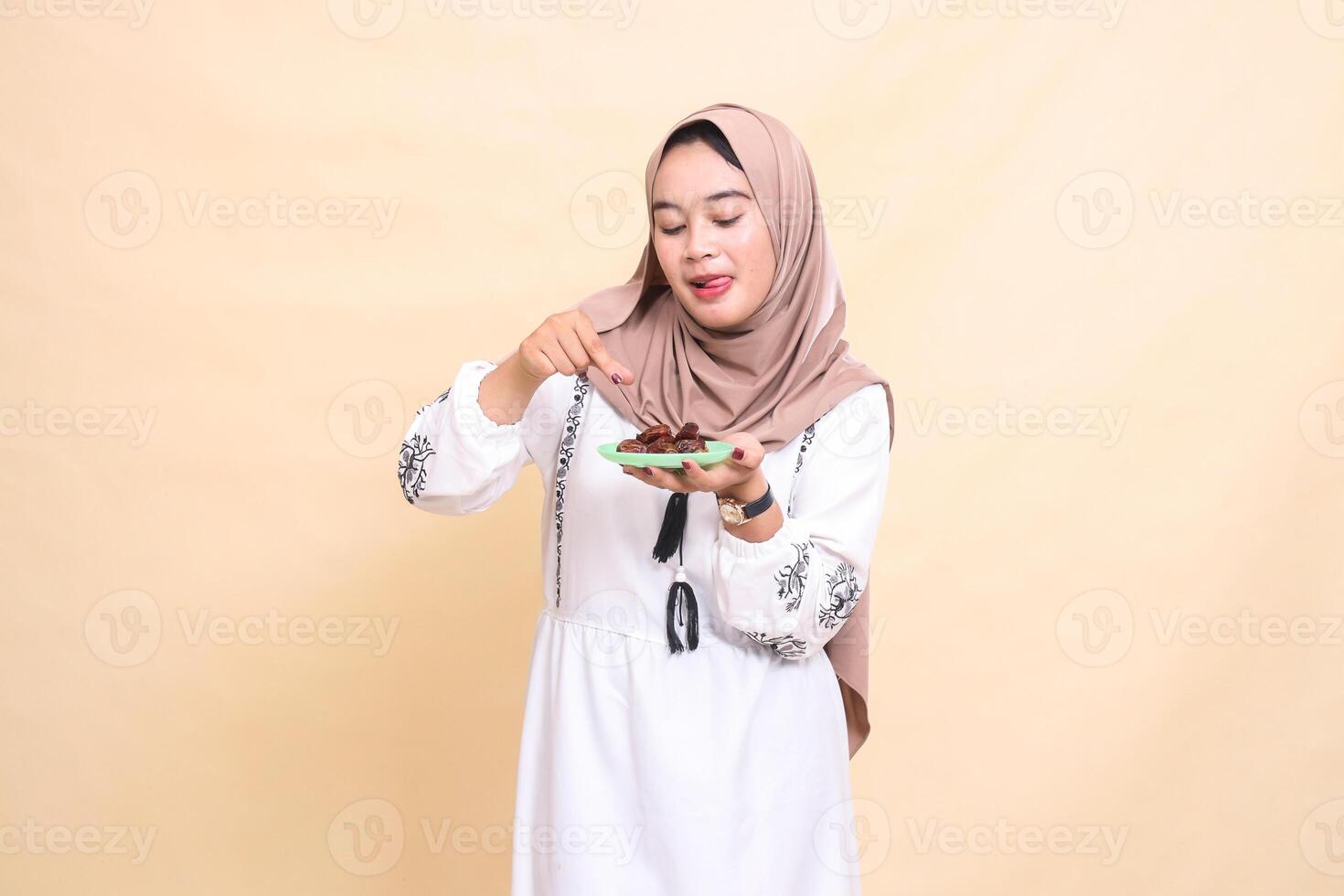 A beautiful indonesia Muslim woman wearing a hijab with a delicious expression picks and brings some dates for the meal and breaking the fast. used for advertising, health, Eid and Ramadan photo