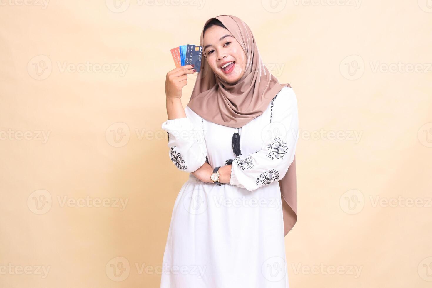 a beautiful indonesia Muslim woman wearing a hijab with a cheerful smile and her arms holding a debit credit card to her side for payment. used for advertising, technology, Eid and Ramadan photo