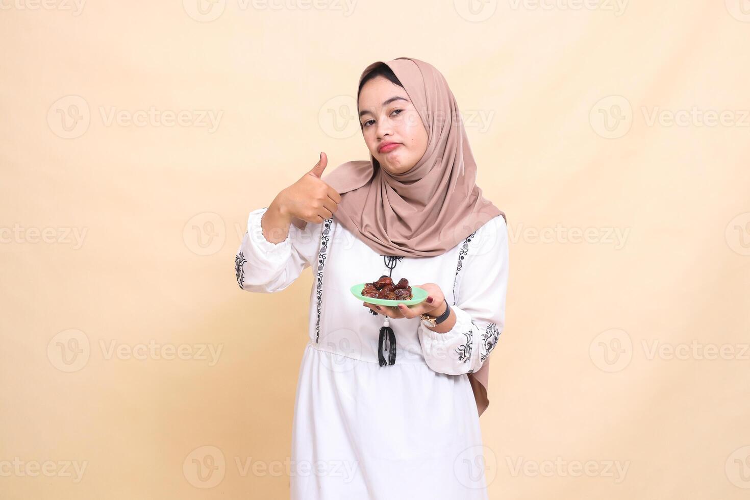 a beautiful indonesia Muslim woman in a hijab pouted with a thumbs up gesture okay good and brought some dates for the sahur menu and breaking the fast. used for advertising, health, Eid and Ramadan photo