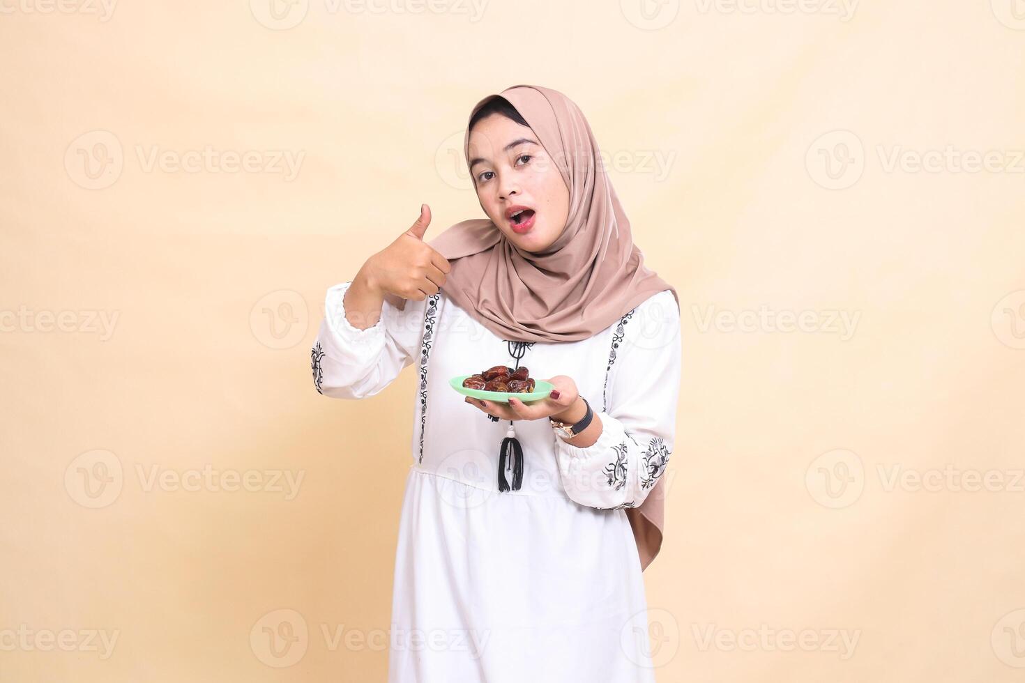 A beautiful Asian Muslim woman wearing a hijab was surprised to give a thumbs up gesture and brought some dates for sahur and breaking the fast. used for advertising, health, Eid and Ramadan photo