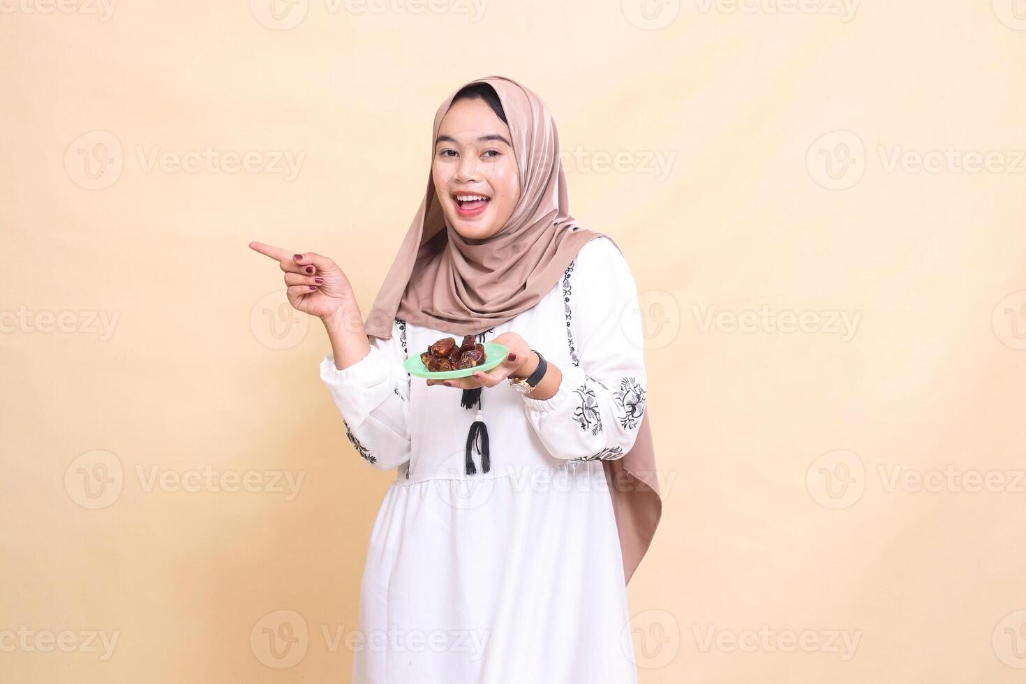 a beautiful indonesia Muslim girl wearing a hijab likes to point to the right and bring dates for the sahur menu and breaking the fast. used for advertising, health, Eid and Ramadan photo