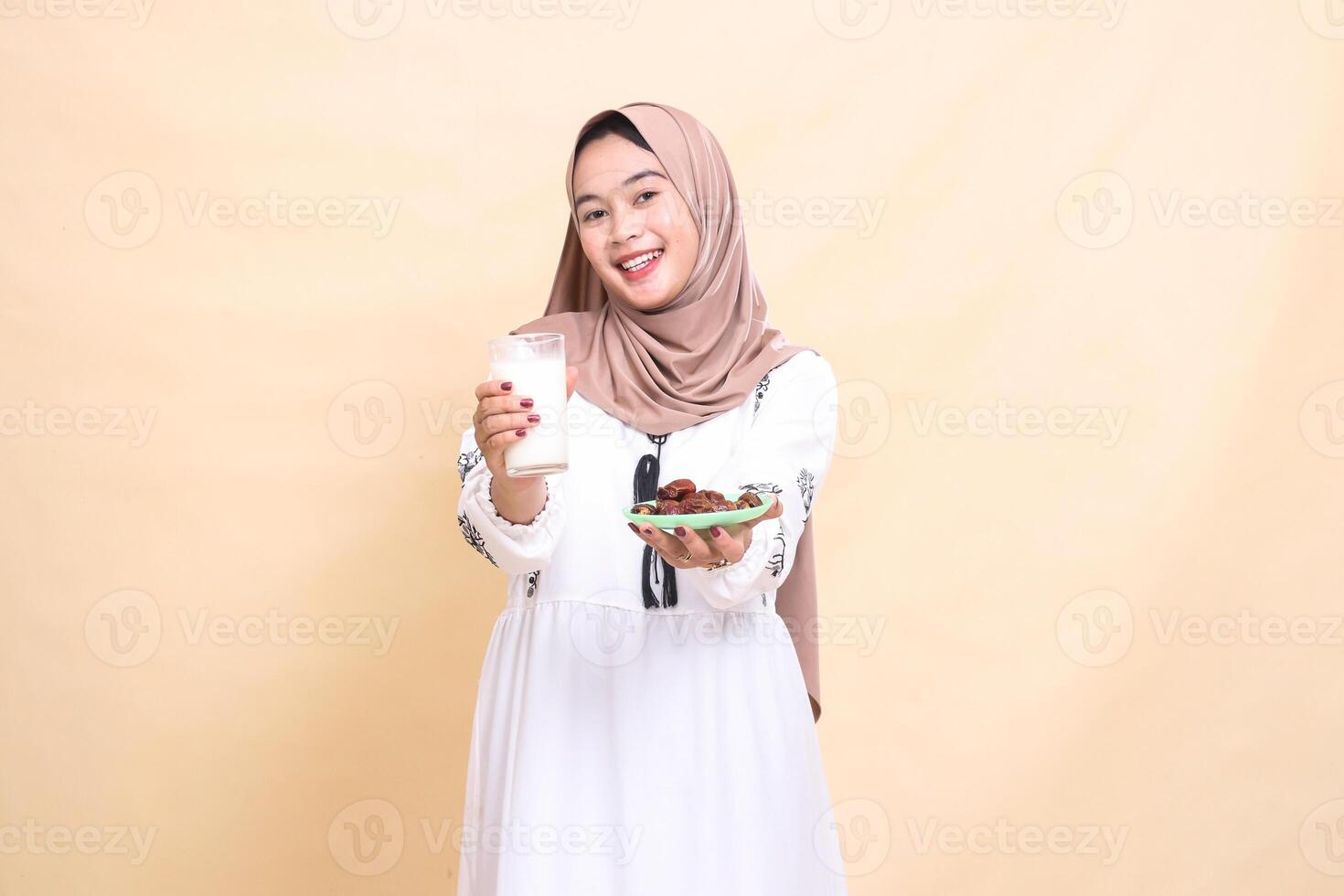 a beautiful indonesia Muslim woman wearing a hijab with a cheerful smile brings a glass of milk and dates forward to break the fast. used for advertising, health, Eid and Ramadan photo
