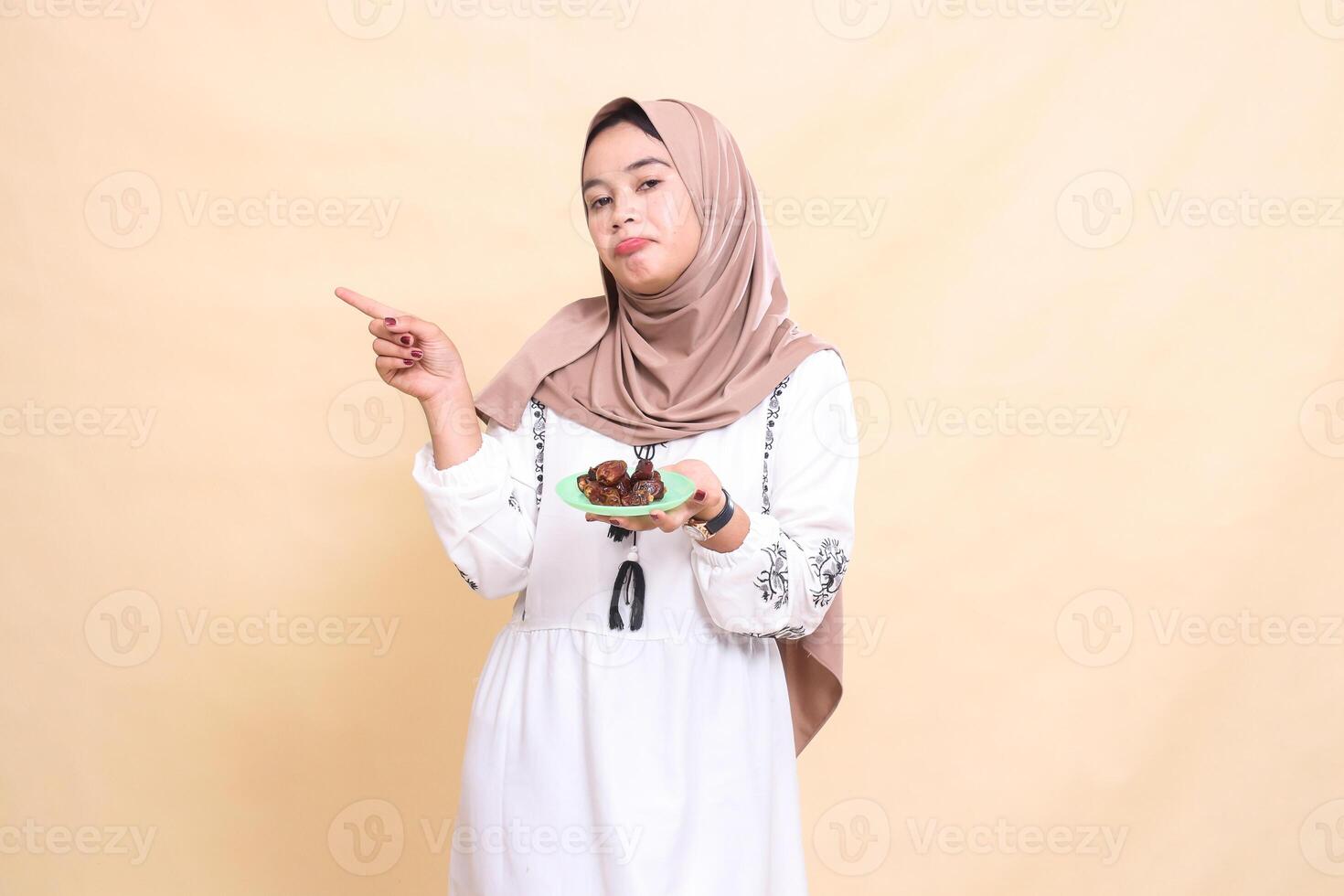 a beautiful Asian Muslim woman wearing a hijab pouted, pointing to the right and carrying dates for the sahur menu and breaking the fast. used for advertising, health, Eid and Ramadan photo
