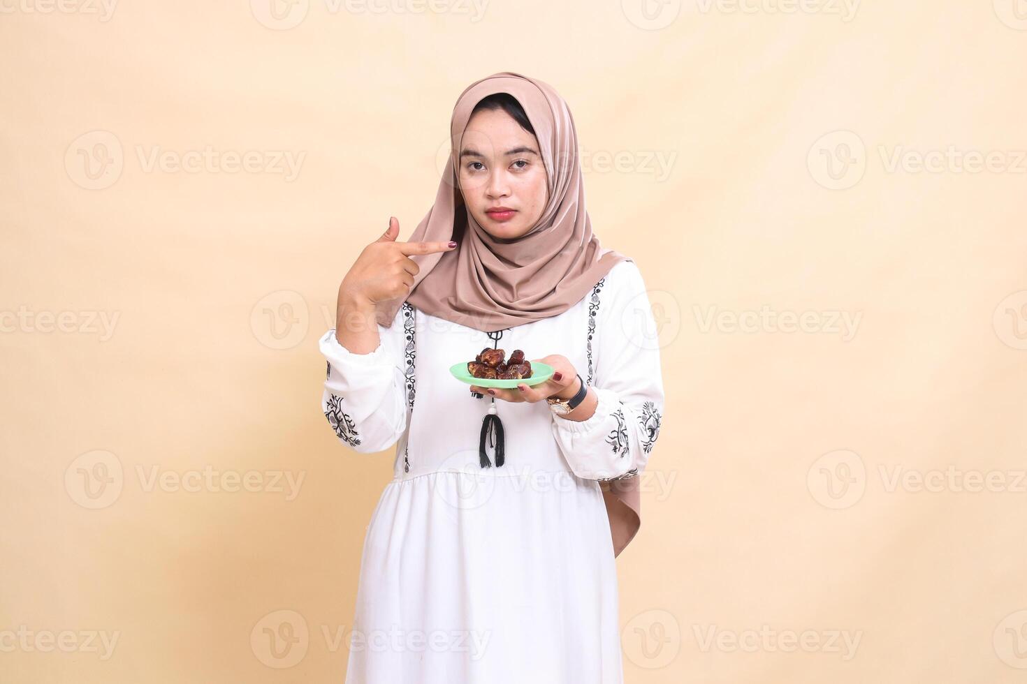 a beautiful indonesia Muslim woman wearing a hijab angrily points to the left and brings dates for the sahur menu and breaking the fast. used for advertising, health, Eid and Ramadan photo