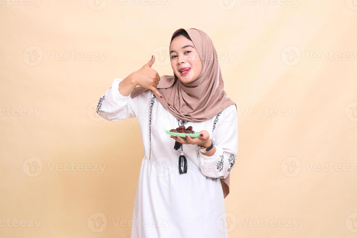 a beautiful Asian Muslim woman wearing a hijab with a delicious expression signals the phone and brings some dates for the meal and breaking the fast. used for advertising, health, Eid and Ramadan photo