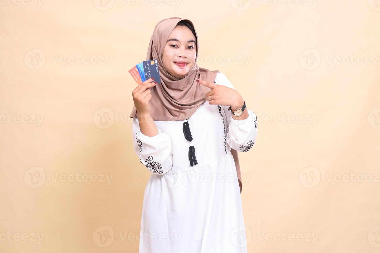 a beautiful Asian Muslim woman wearing a hijab smiles pointing to the debit credit on the right side for payment. used for advertising, technology, Eid and Ramadan photo