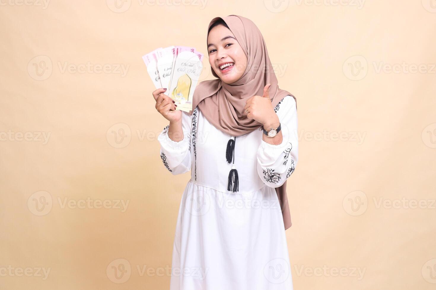 portrait of a beautiful Asian Muslim girl wearing a hijab smiling wearing a hijab holding and showing off gifts and gifts to the right on Eid. used for advertising, giveaways, Eid and Ramadan photo