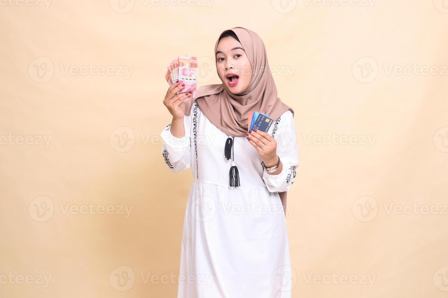 a beautiful indonesia Muslim woman wearing a hijab is surprised to bring rupiah money and a debit credit card for payment. used for advertising, technology, Eid and Ramadan photo