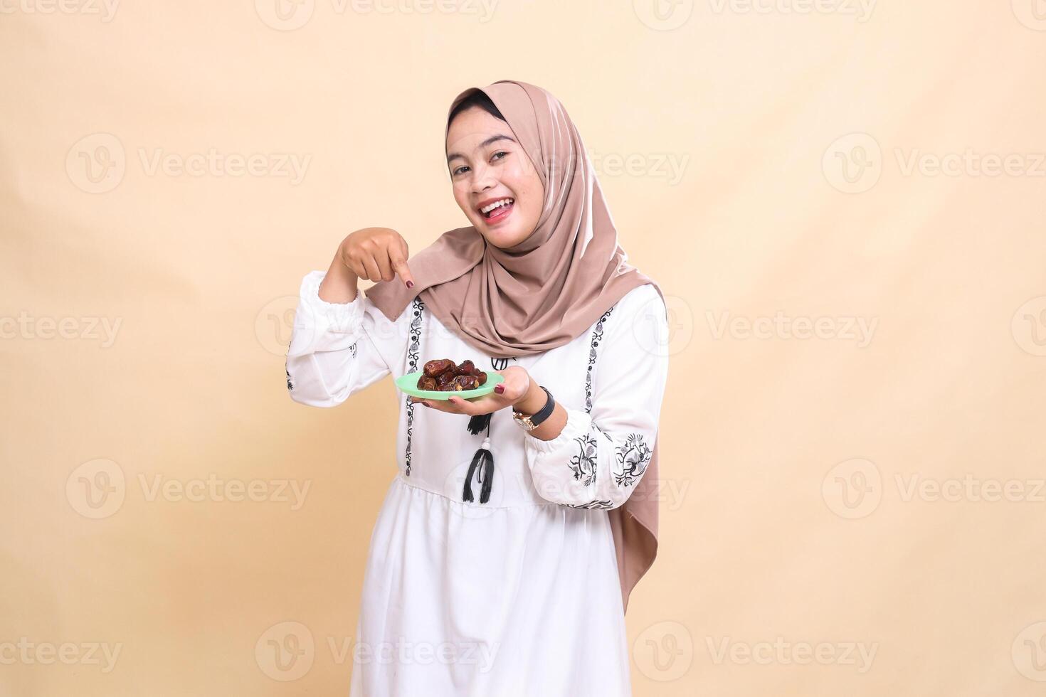 a beautiful Asian Muslim woman wearing a hijab smiles carrying and pointing to dates for the sahur menu and breaking the fast. used for advertising, health, Eid and Ramadan photo