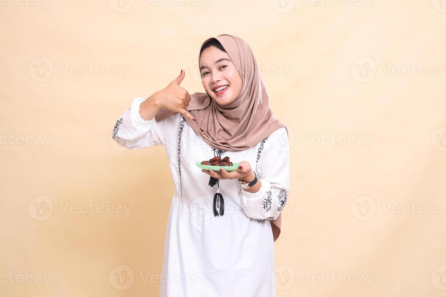 A beautiful Asian Muslim woman wearing a hijab smiles cheerfully at the phone and brings some dates for the meal and breaking the fast. used for advertising, health, Eid and Ramadan photo