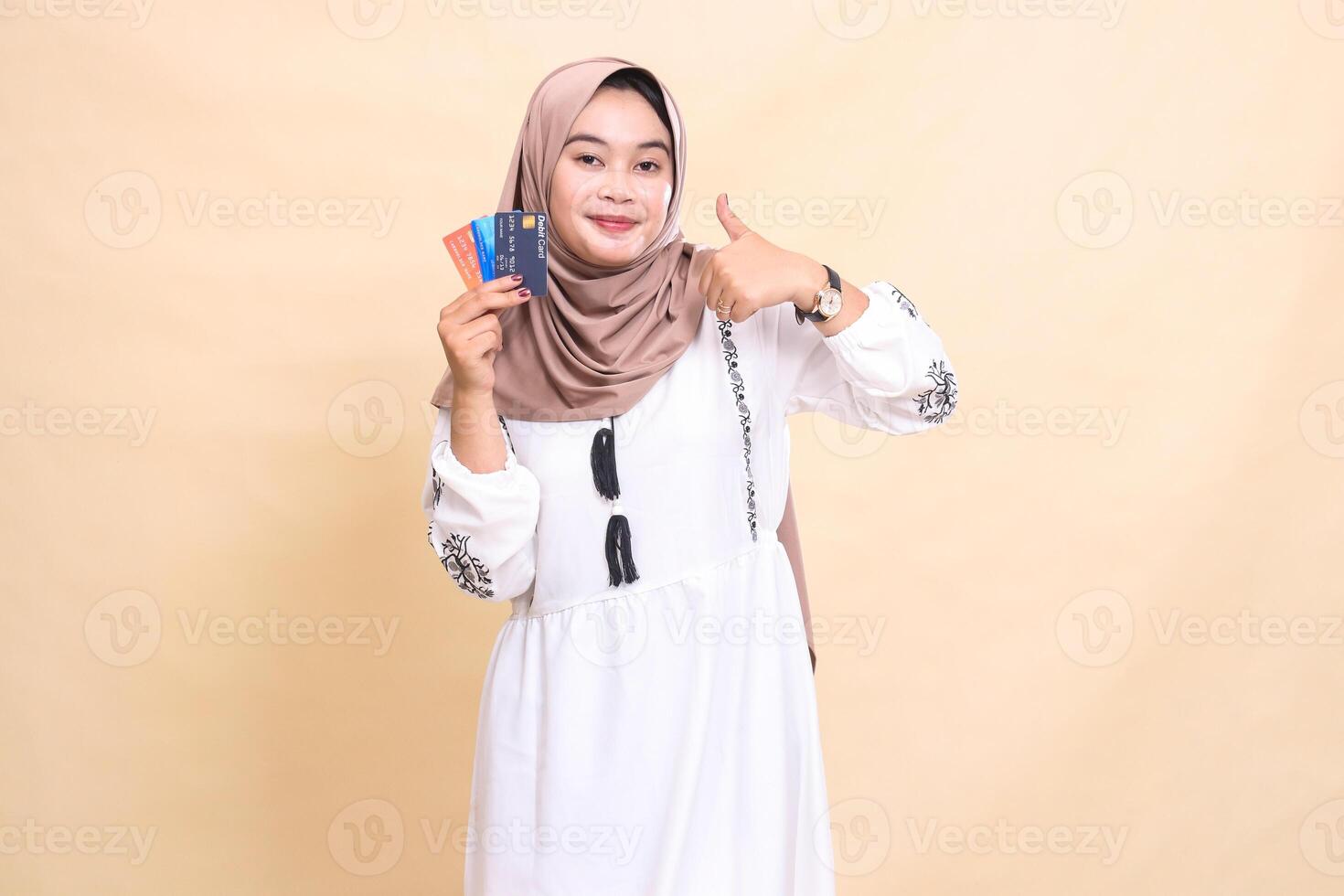 a beautiful Asian Muslim woman wearing a hijab smiles with a thumbs up gesture okay and carries a debit credit card for online offline payments. used for advertising, technology, Eid and Ramadan photo