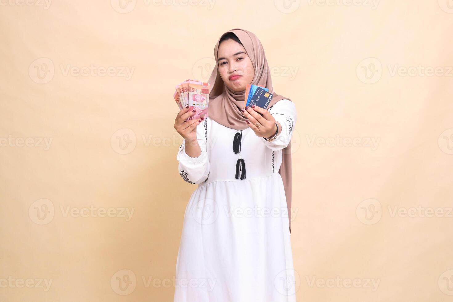a beautiful Asian Muslim girl in a hijab sullenly carries rupiah money and advances a debit credit card for payment. used for advertising, technology, Eid and Ramadan photo