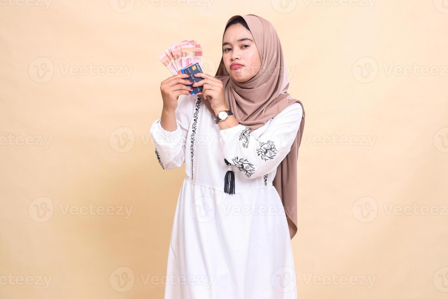 a beautiful indonesia Muslim woman wearing a sullen hijab brings to her right side rupiah notes and a debit credit card for payment. used for advertising, technology, Eid and Ramadan photo