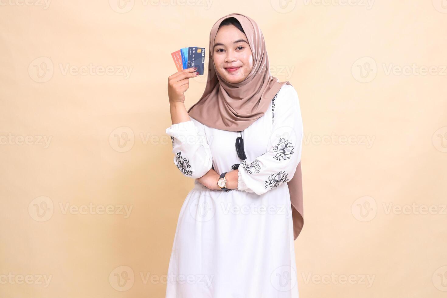 a beautiful Asian Muslim woman wearing a hijab with a graceful smile with her arms crossed carrying a debit credit card to her side for payment. used for advertising, technology, Eid and Ramadan photo