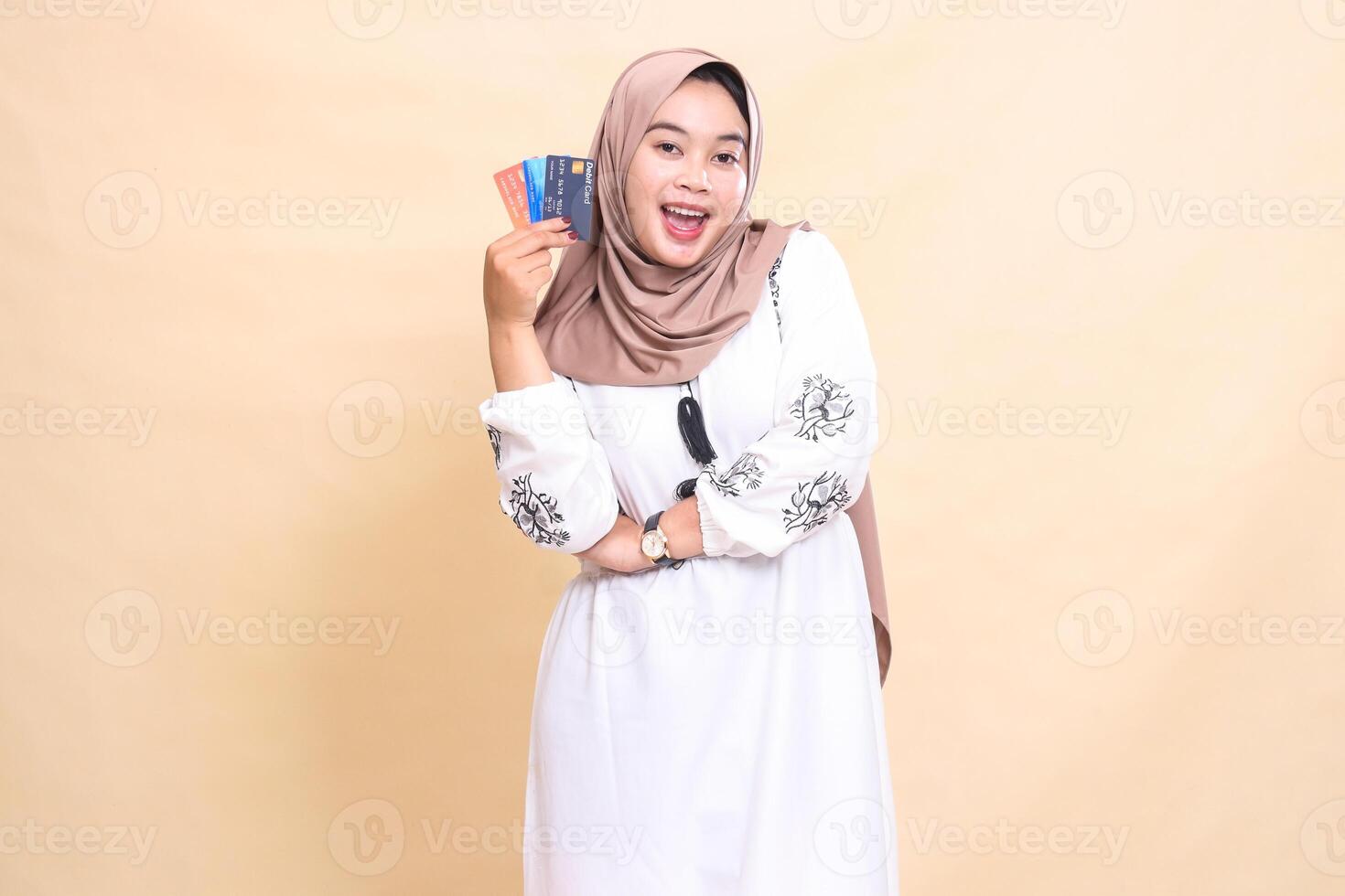 a beautiful Asian Muslim woman wearing a happy hijab with her arms crossed carrying a debit credit card to her side for payment. used for advertising, technology, Eid and Ramadan photo