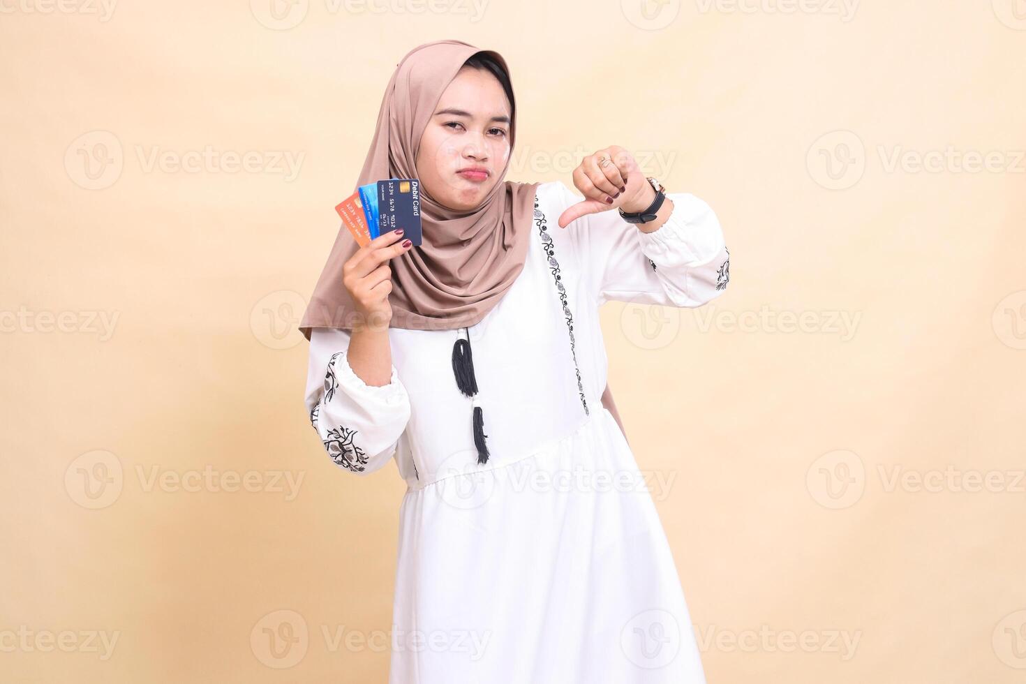 a beautiful Asian Muslim woman in a hijab frowns with a thumbs up gesture and carries a debit credit card for offline online payments. used for advertising, technology, Eid and Ramadan photo