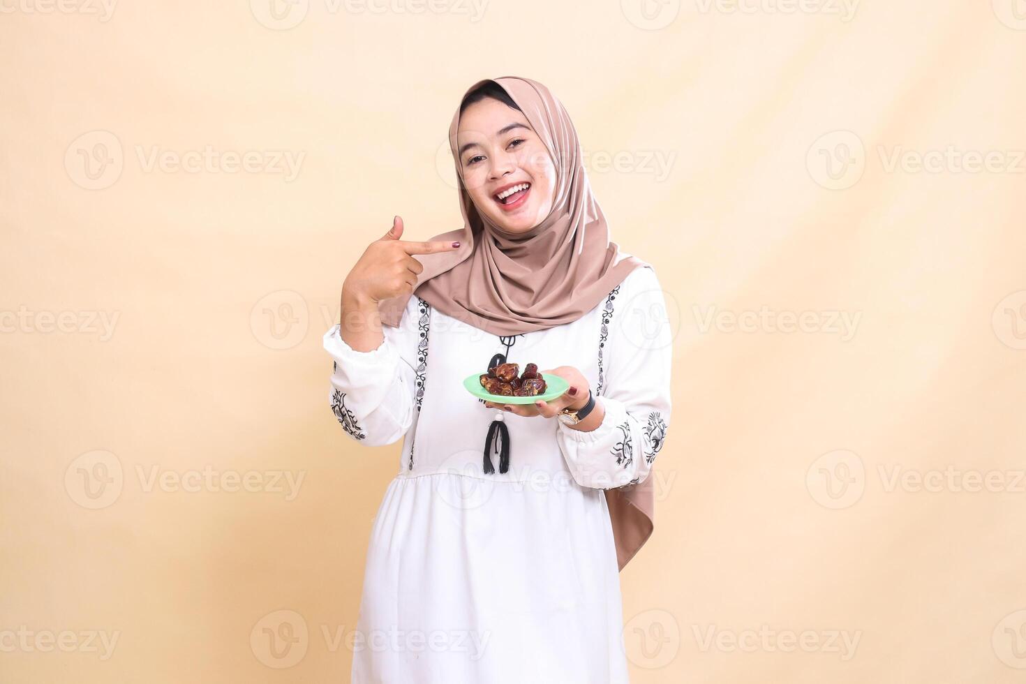 a beautiful indonesia Muslim woman wearing a hijab smiles cheerfully pointing to the left and carrying dates for the sahur menu and breaking the fast. used for advertising, health, Eid and Ramadan photo