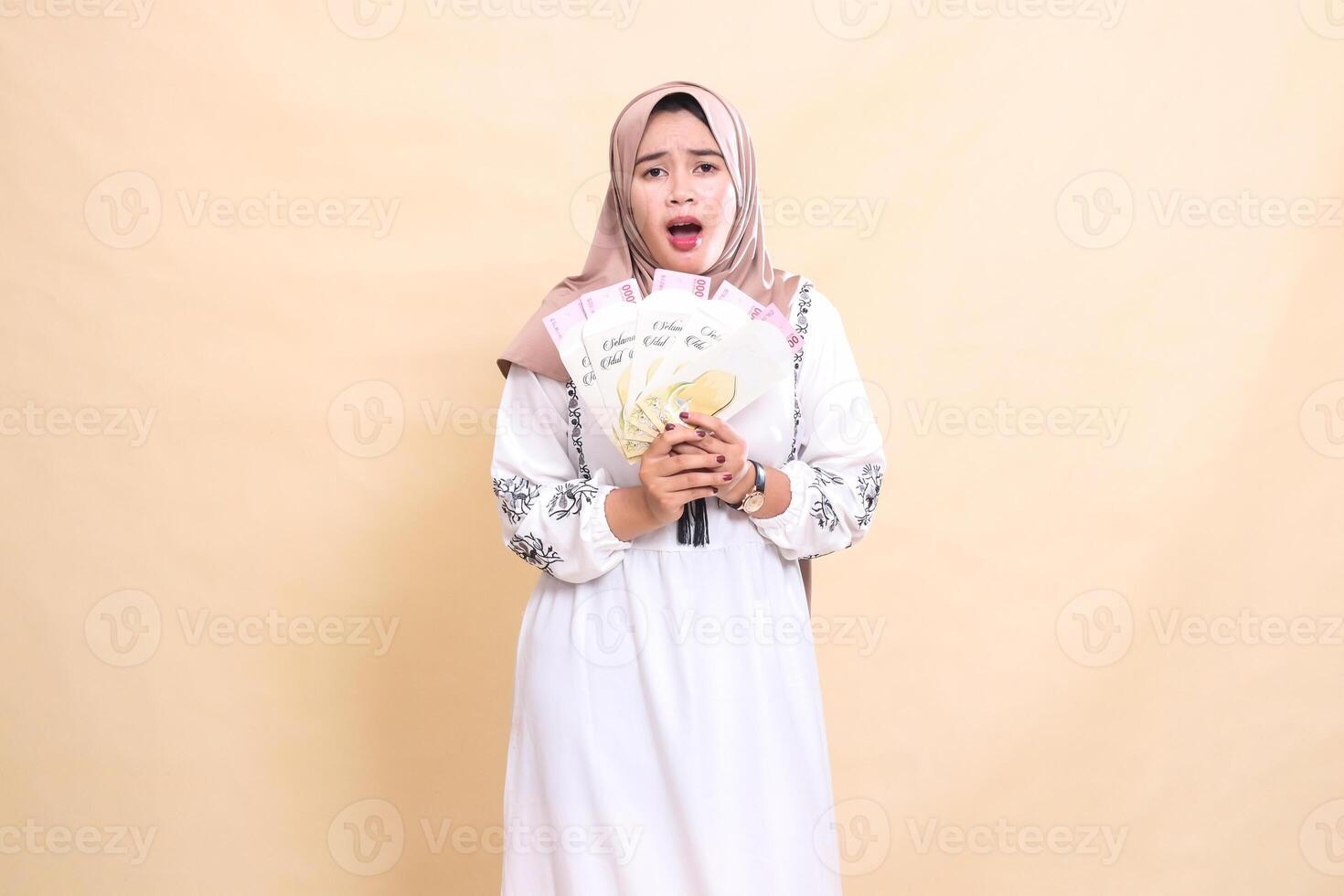 portrait of a beautiful Asian Muslim woman wearing a hijab, shocked and sad, holding a gift or fitrah on Eid. used for advertising, giveaways, Eid and Ramadan photo