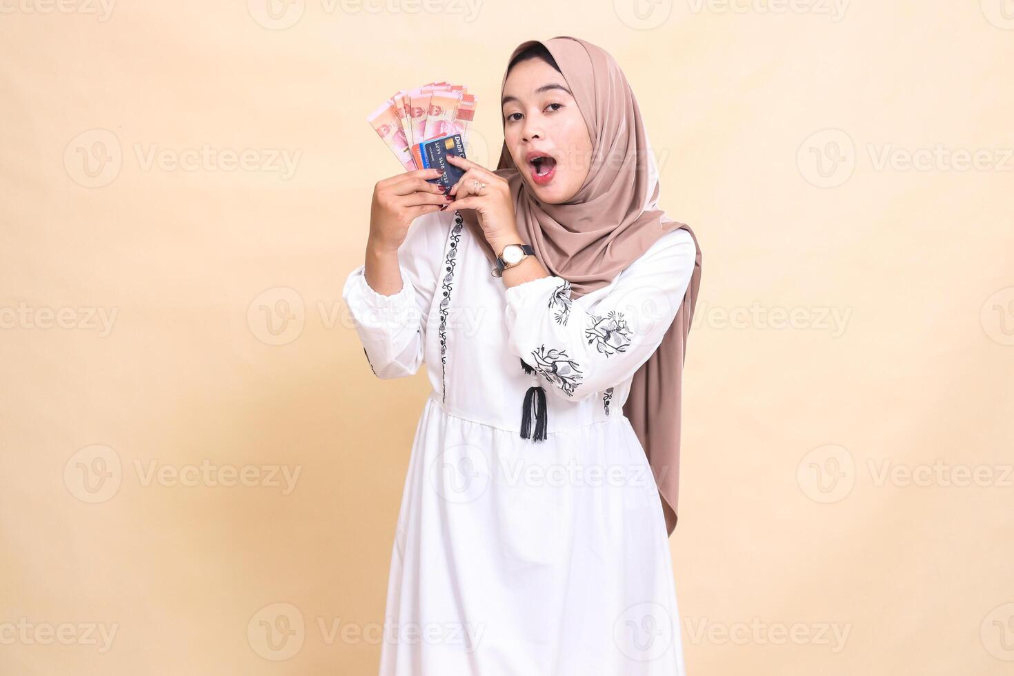 a beautiful Asian Muslim woman wearing a hijab was surprised to bring to her right side rupiah notes and a debit credit card for payment. used for advertising, technology, Eid and Ramadan photo