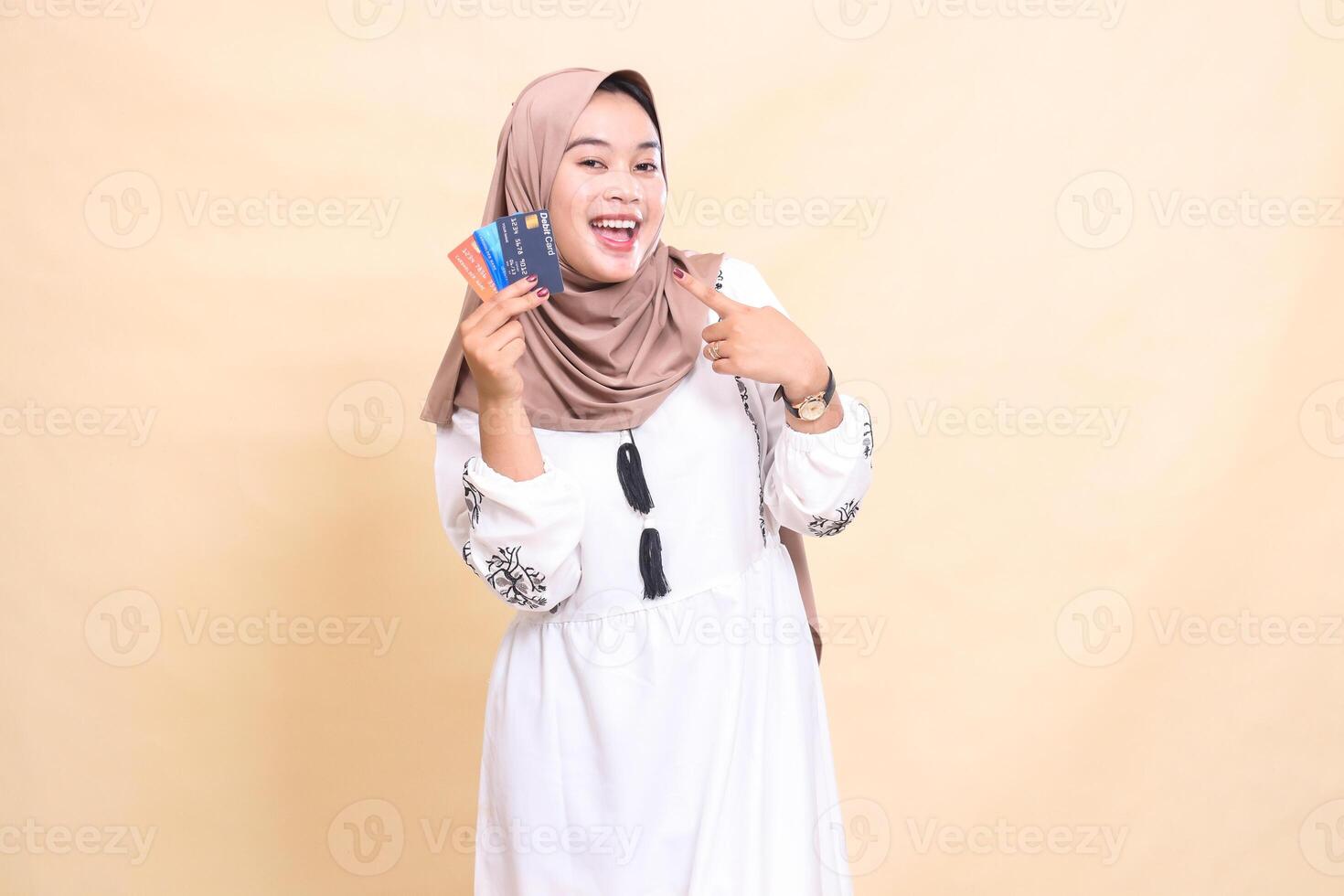 a beautiful indonesia Muslim woman wearing a hijab smiles cheerfully pointing to the debit credit on the right side for payment. used for advertising, technology, Eid and Ramadan photo