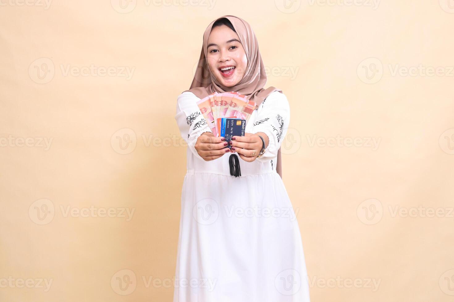 a beautiful Asian Muslim woman wearing a happy hijab brings forward rupiah money and a debit credit card for payment. used for advertising, technology, Eid and Ramadan photo