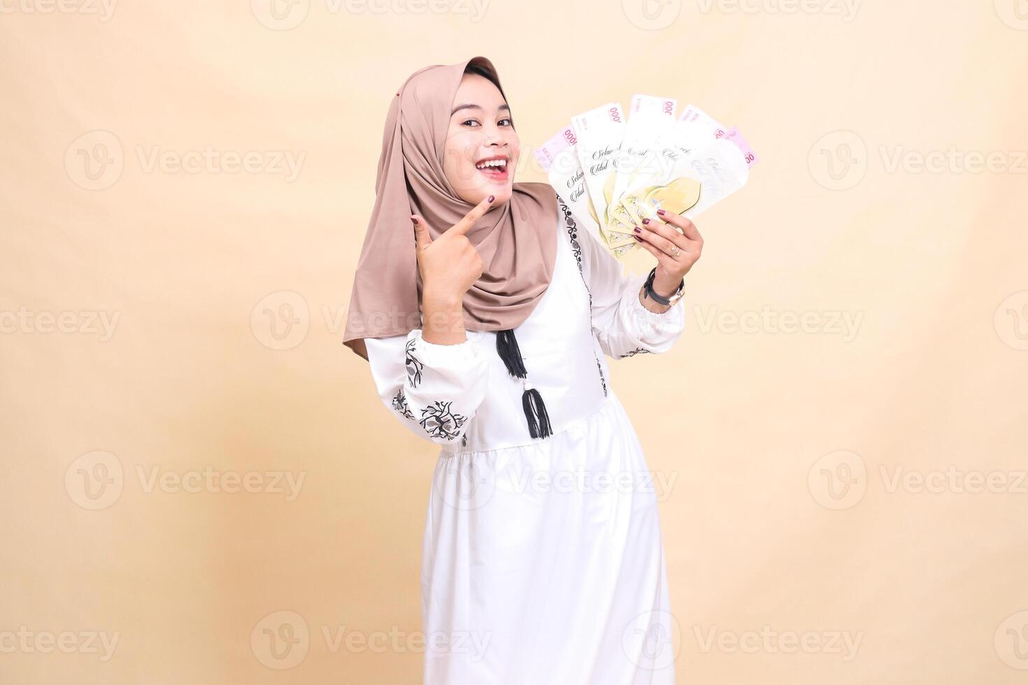 Portrait of a beautiful Asian Muslim woman wearing a cheerful hijab holding and showing gifts and gifts to the left on Eid day. used for advertising, giveaways, Eid and Ramadan photo
