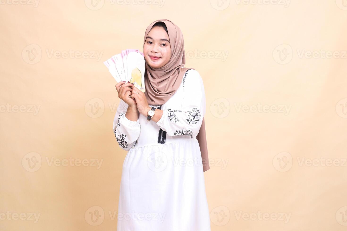 portrait of a beautiful Asian Muslim girl wearing a hijab smiling gracefully, holding and showing off gifts and gifts to the right on Eid day. used for advertising, giveaways, Eid and Ramadan photo