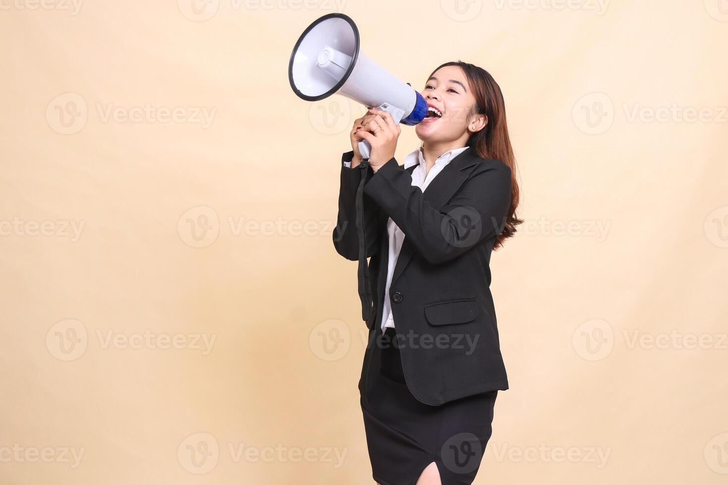 Beautiful formal indonesia office woman in suit standing happy shouting up using megaphone for promo broadcast announcement on yellow background for commercial, advertising and business photo