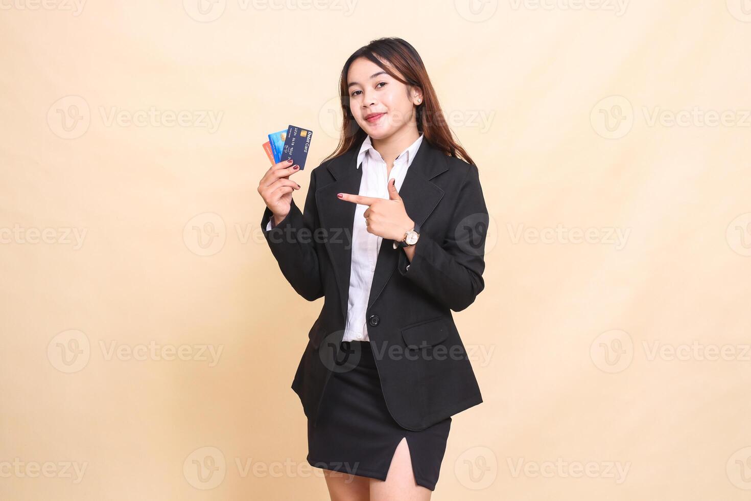 Beautiful formal Asian office woman in suit standing elegantly carrying debit credit card and pointing at it for easy transaction on yellow background for commercial, vacancy and business photo