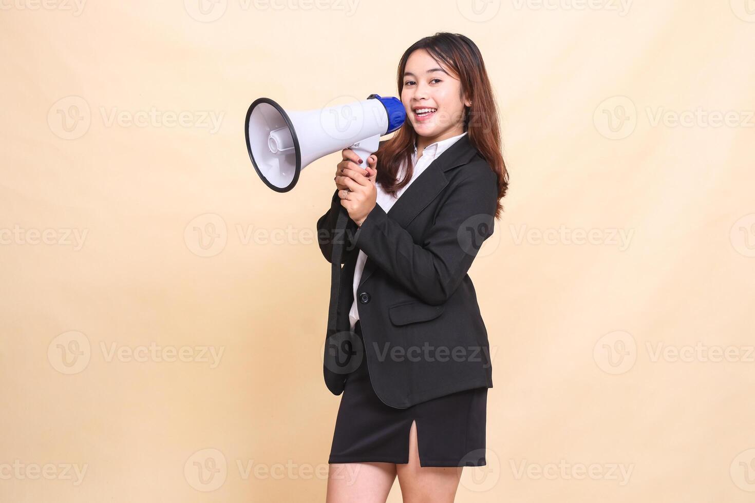 Beautiful formal Asian office woman in suit standing happy to camera holding megaphone for broadcast announcement on yellow background for commercial, advertising and business photo