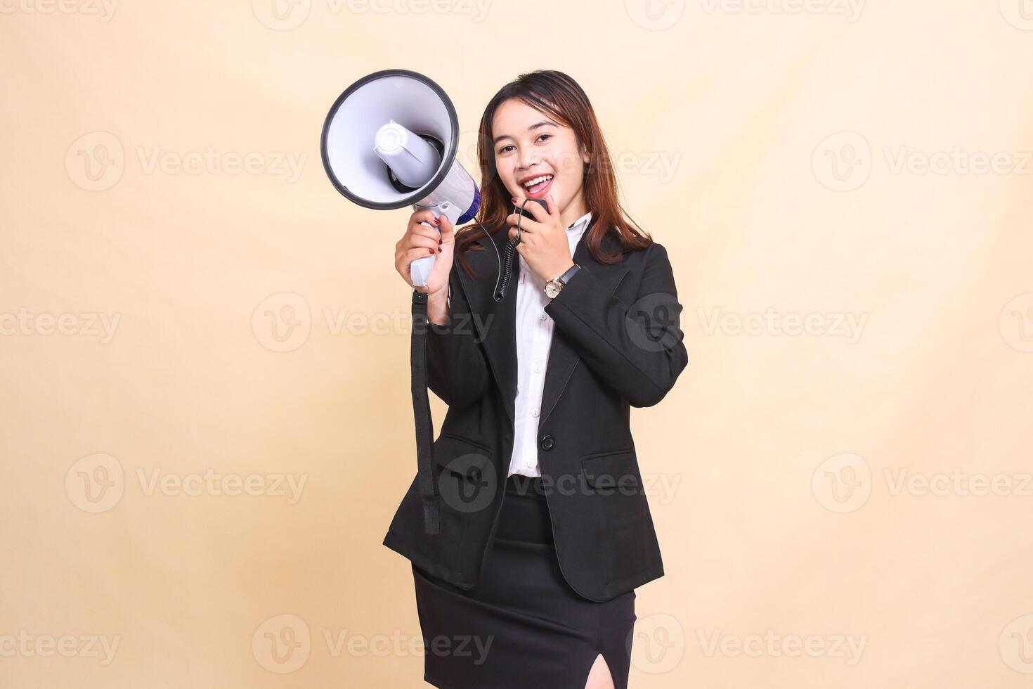 Beautiful formal Asian office woman in suit standing smile shouting into camera with mic using megaphone for promo broadcast announcement on yellow background for commercial, advertising and business photo