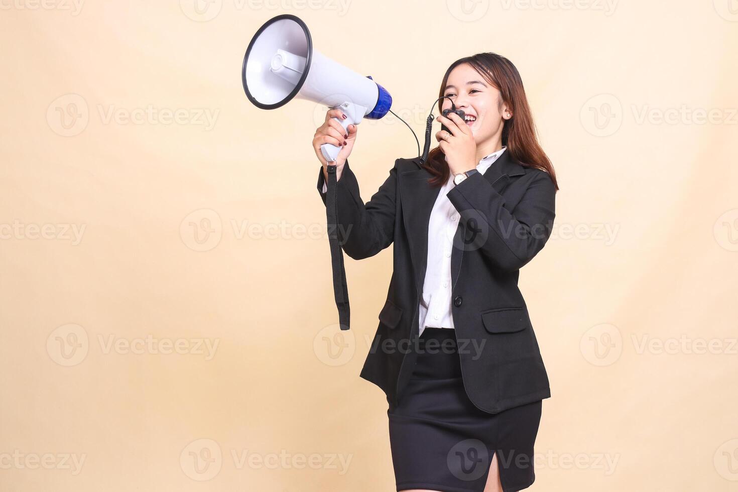 Beautiful formal Asian office woman in suit standing shouting with mic using megaphone for promo broadcast announcement on yellow background for commercial, advertising and business photo