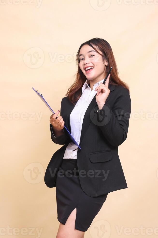 Beautiful formal indonesia executive mature woman in suit can idea stand and pose bring clipboard pen to camera, 3 by 4 body portrait on yellow background for commercial, vacancy and business photo
