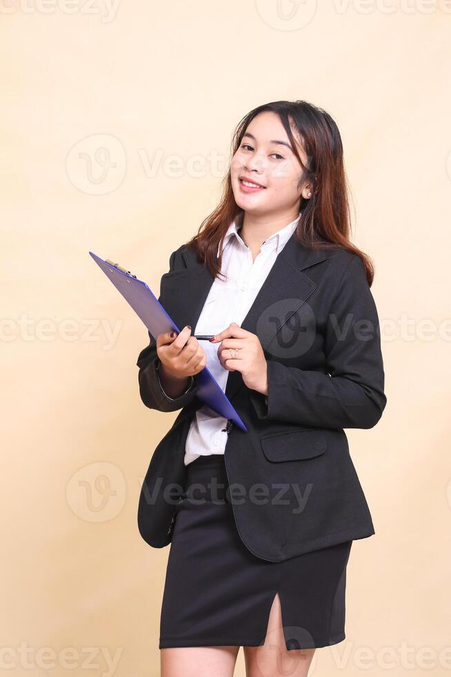 Beautiful formal Asian executive mature woman in suit cheerful smile standing and pose holding clipboard pen to camera, 3 by 4 body portrait on yellow background for commercial, vacancy and business photo