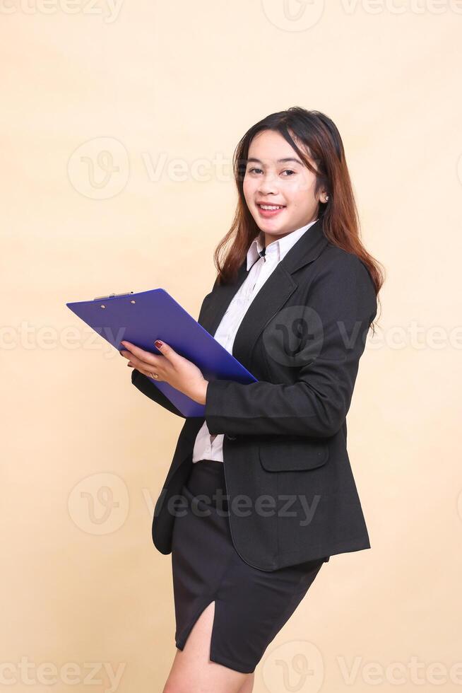 Beautiful formal indonesia executive mature woman in suit happy smile standing and pose holding clipboard to camera, 3 by 4 body portrait on yellow background for commercial, vacancy and business photo