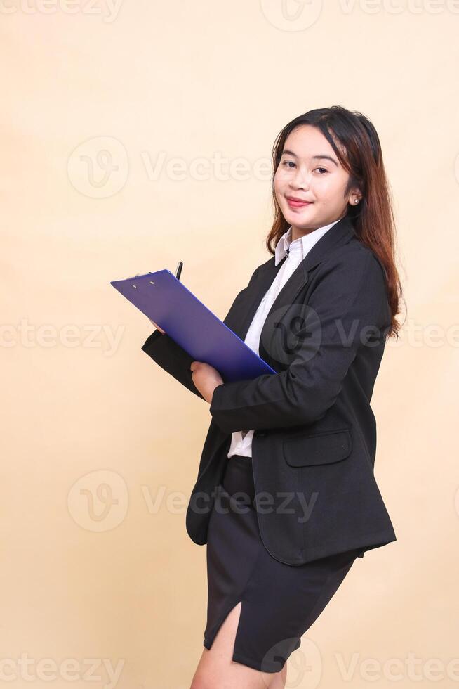 Beautiful formal Asian executive mature woman in suit smiling standing and taking notes pose taking clipboard to camera, 3 by 4 body portrait on yellow background for commercial, vacancy and business photo