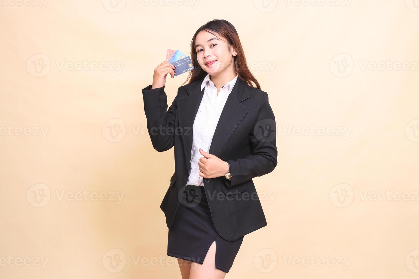 Beautiful formal Asian office woman in suit standing cheerful holding debit credit card and holding jacket for transaction promotion on yellow background for commercial, vacancy and business photo