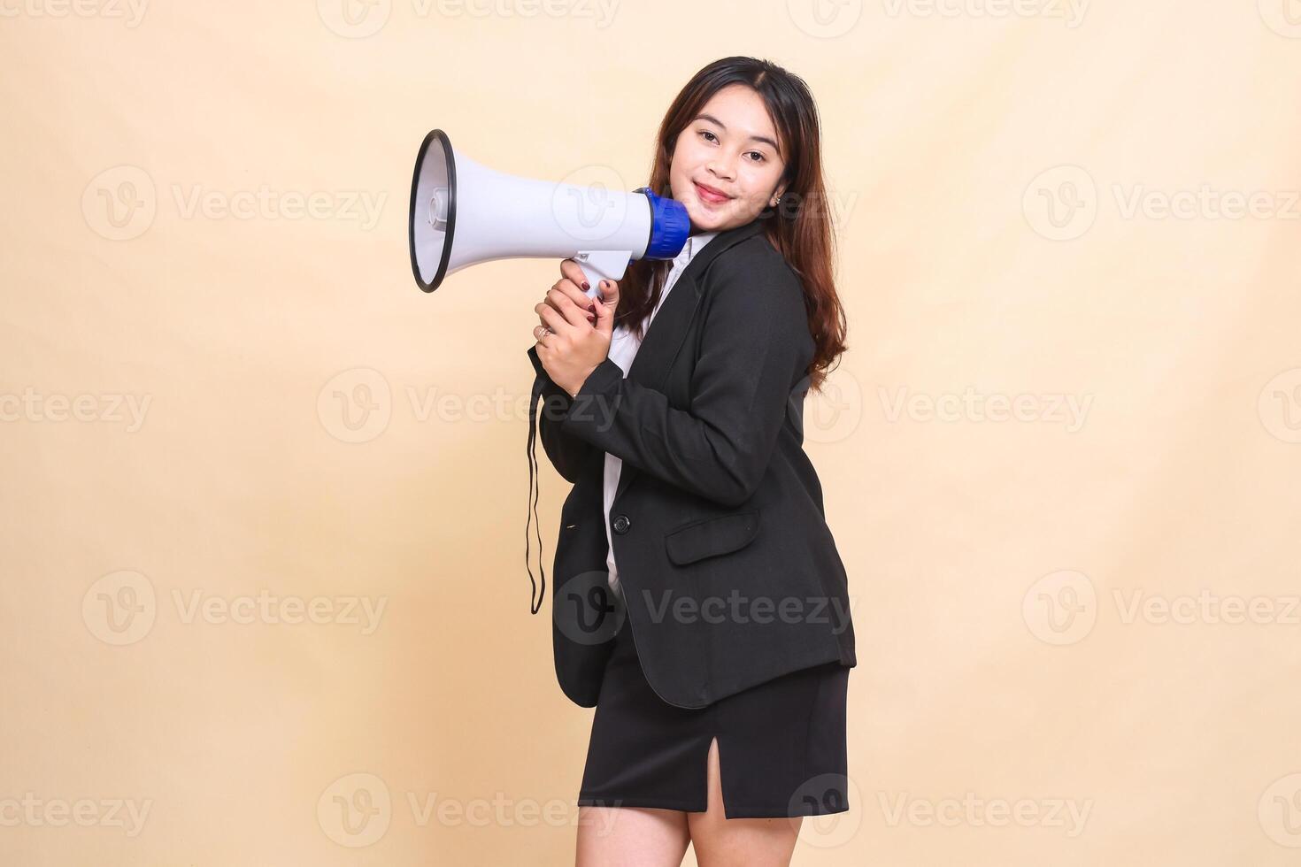 Beautiful formal Asian office woman in suit standing smiling to camera carrying megaphone for broadcast announcement on yellow background for commercial, advertising and business photo