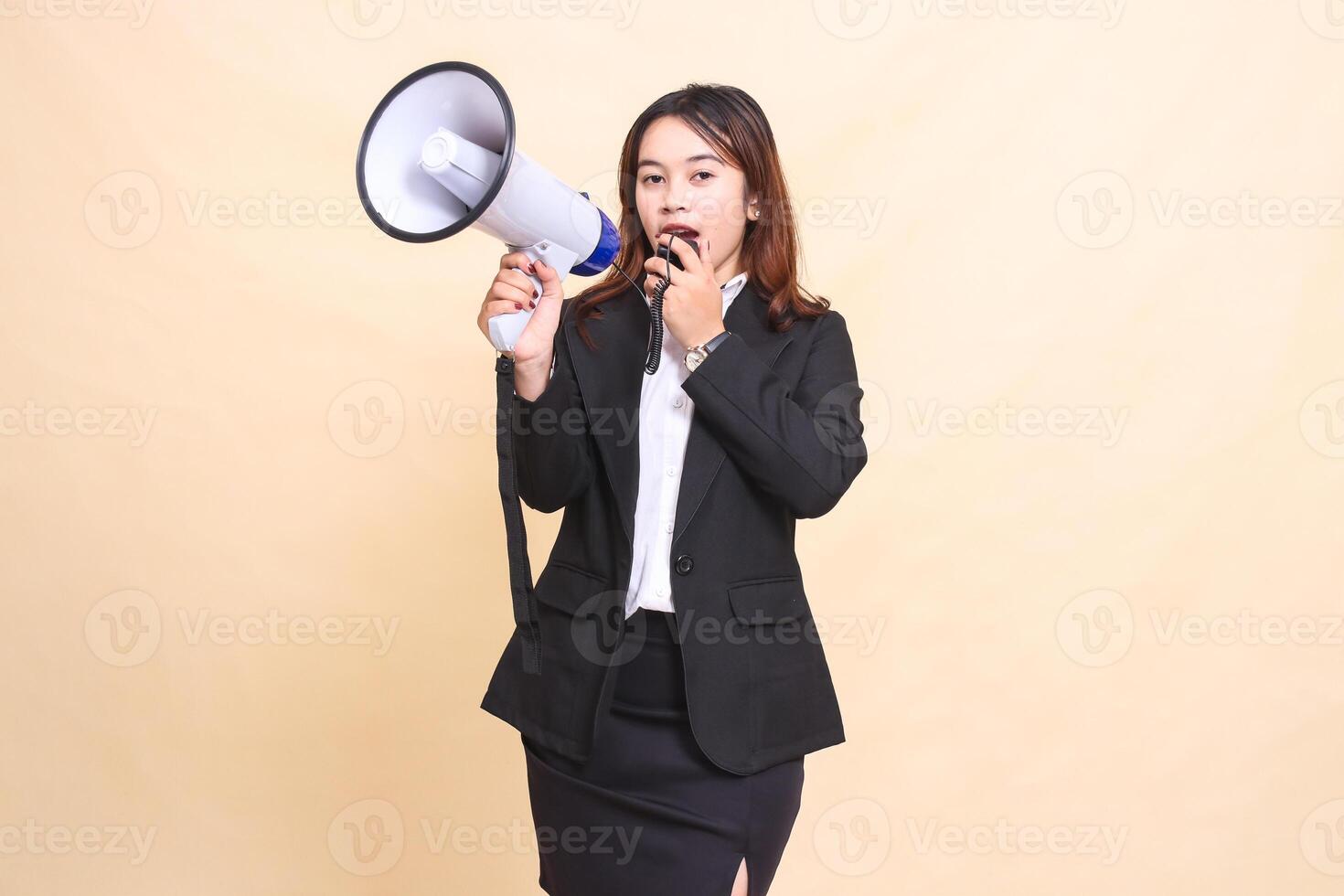 Beautiful formal indonesia office girl in suit standing talking to camera with mic using megaphone for promo broadcast announcement on yellow background for commercial, advertising and business photo