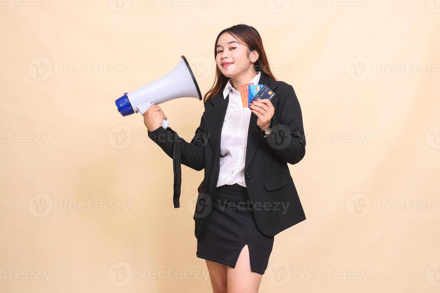 Beautiful formal Asian office woman in suit standing smiling holding debit credit card and megaphone for broadcast announcement on yellow background for commercial, broadcasting and business photo