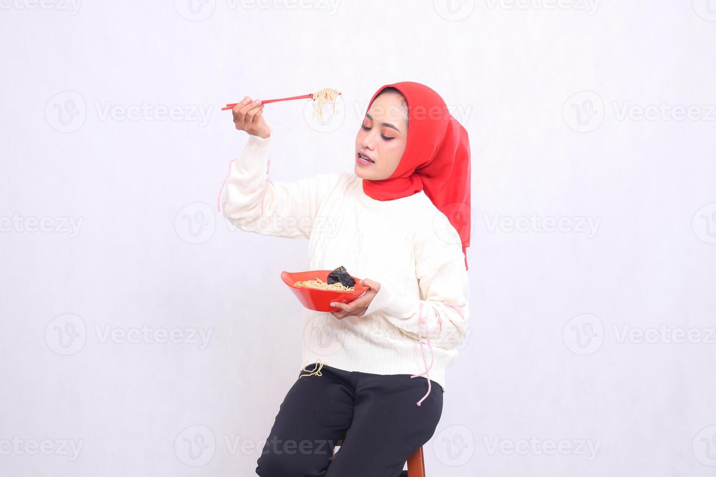 candid asian woman wearing hijab looking down holding noodles with chopsticks from the side and bowl containing ramen chinese food. Beautiful Muslim women use culinary, food and health content photo