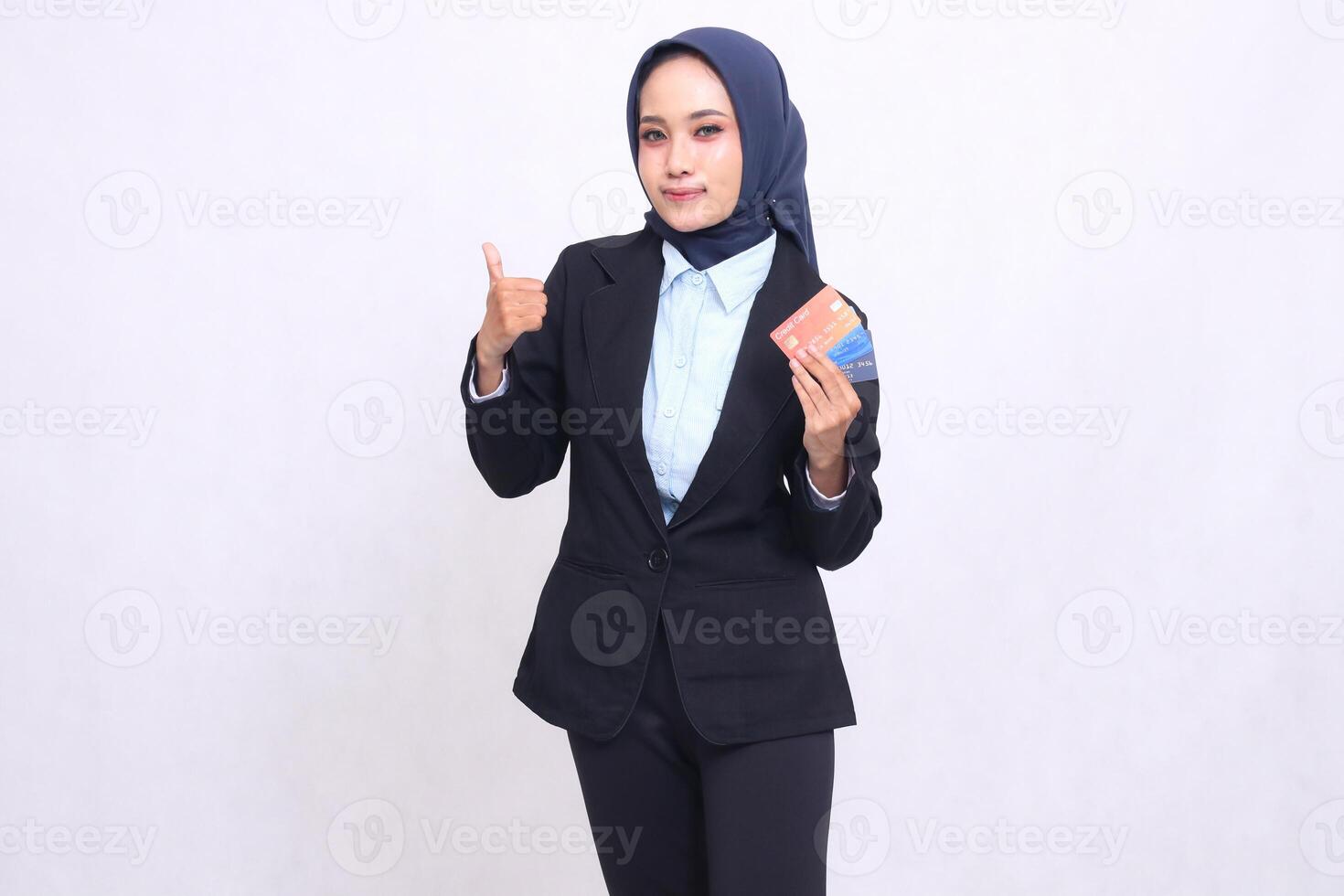 Asian office woman wearing a hijab stands, smiles, gives a thumbs up gesture, OK, good, and brings a debit credit card for easy opening of a bank savings account. Muslim blue shirt for transactions photo
